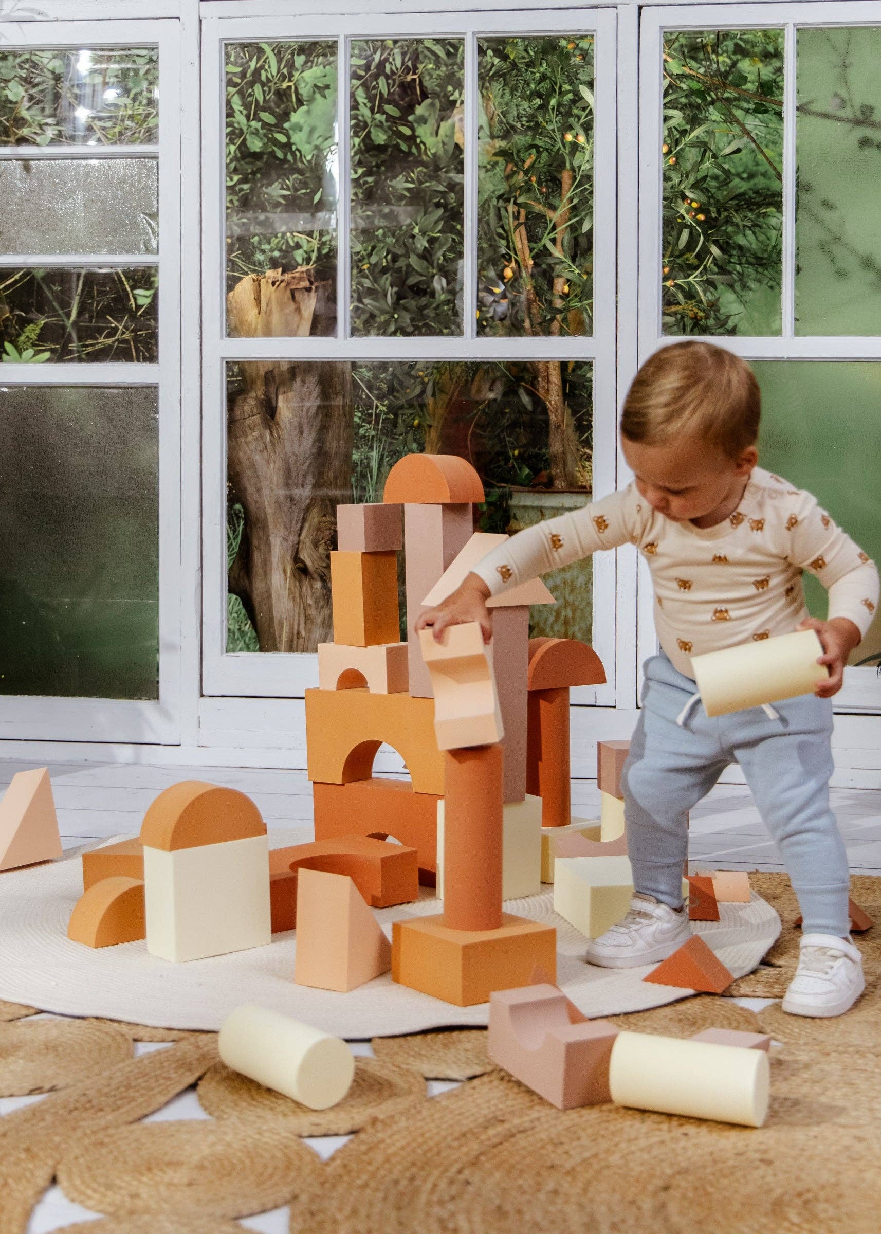 Child playing with wooden building blocks in a room with large windows.