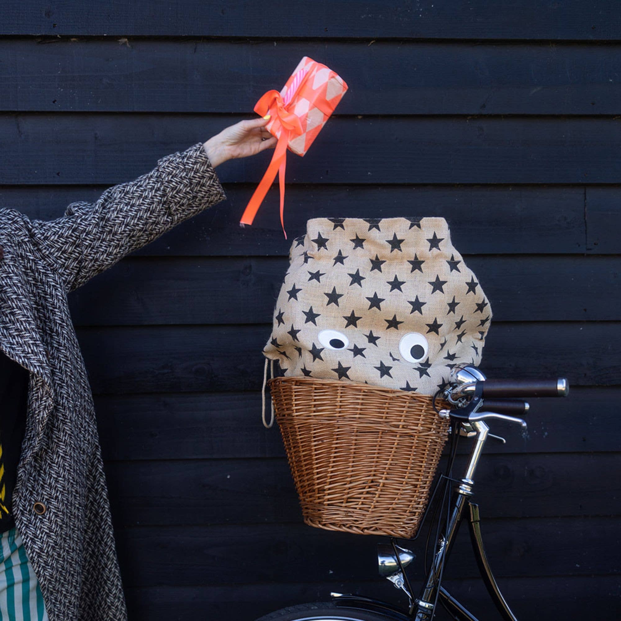 Person holding a gift above a bicycle with a star-patterned basket against a dark wooden wall.