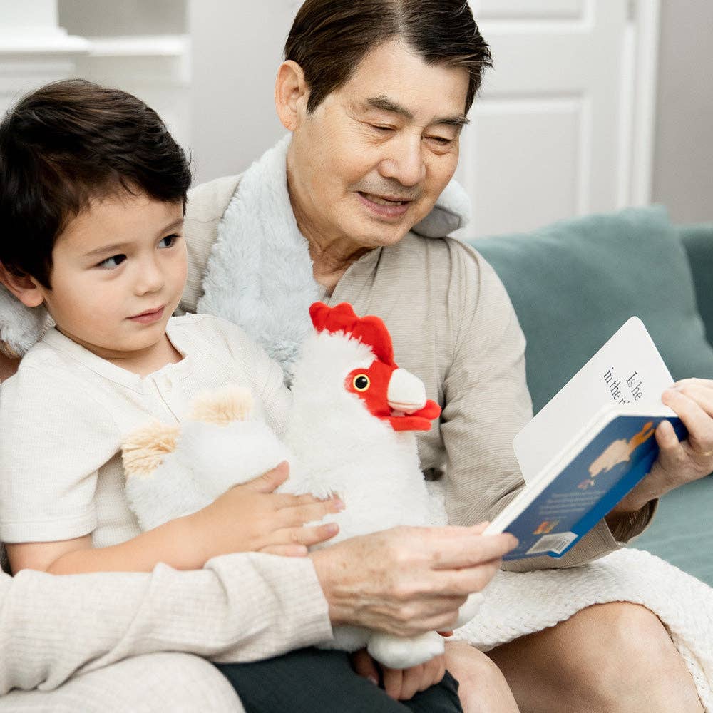 Grandfather and grandson reading a book together with a toy chicken on a couch.