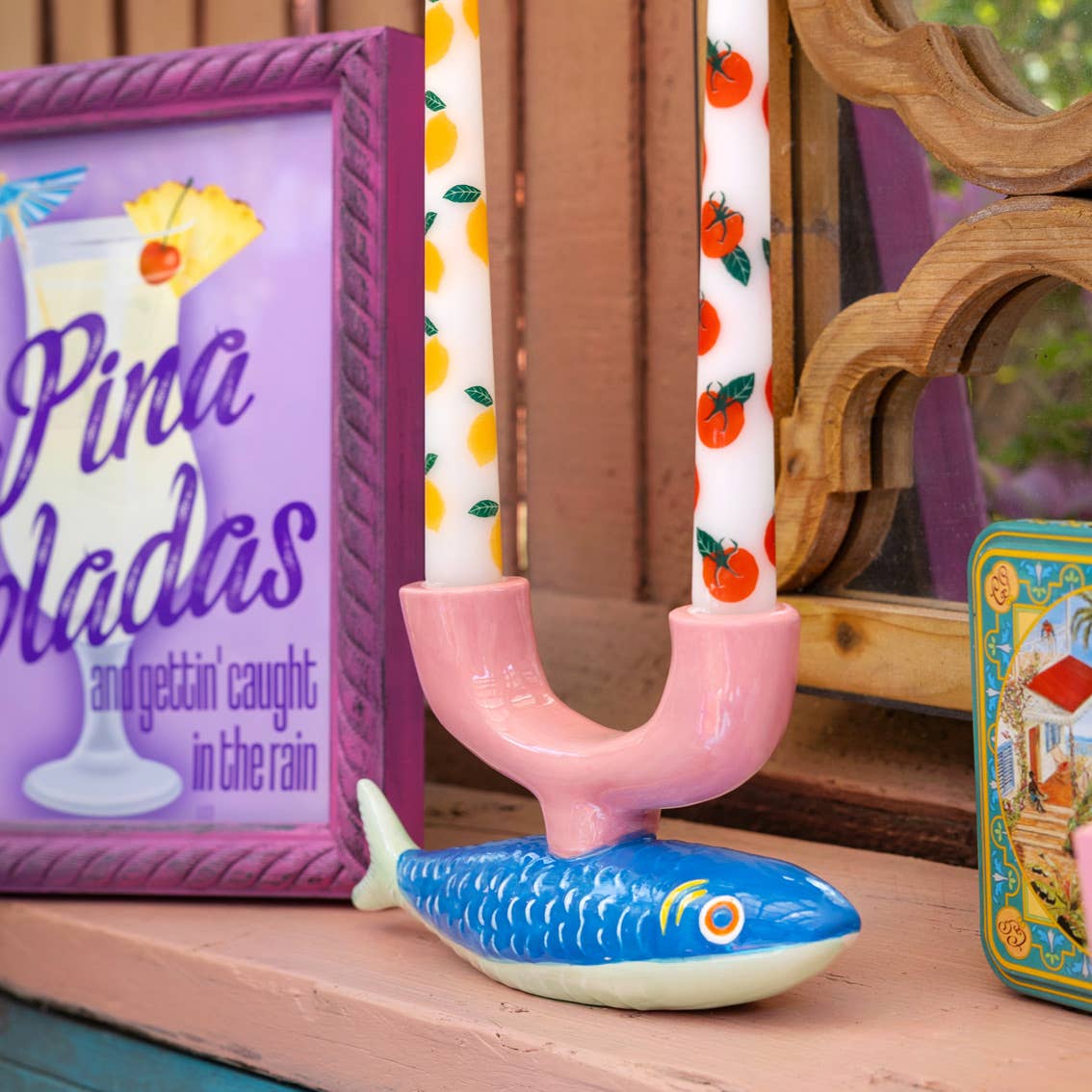 Pink candleholder with candles and a colorful sign on a wooden surface