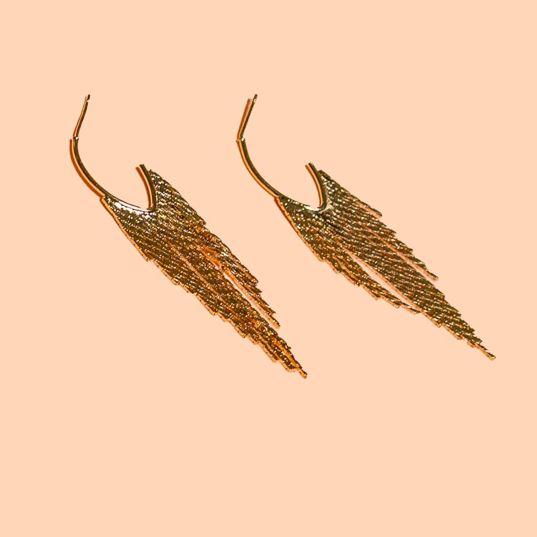 Gold leaf-shaped earrings on a beige background