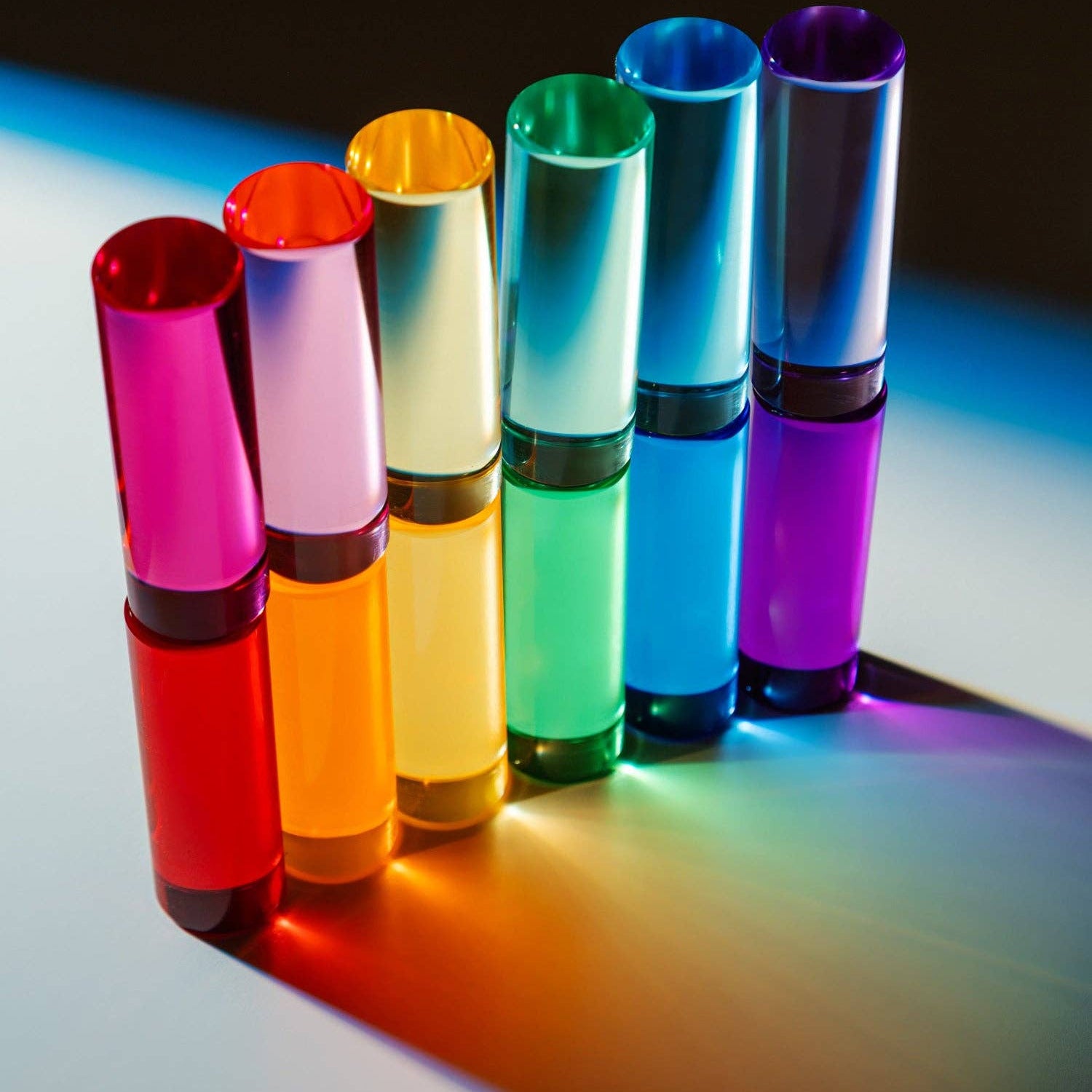 Set of colorful cylindrical objects casting shadows on a reflective surface