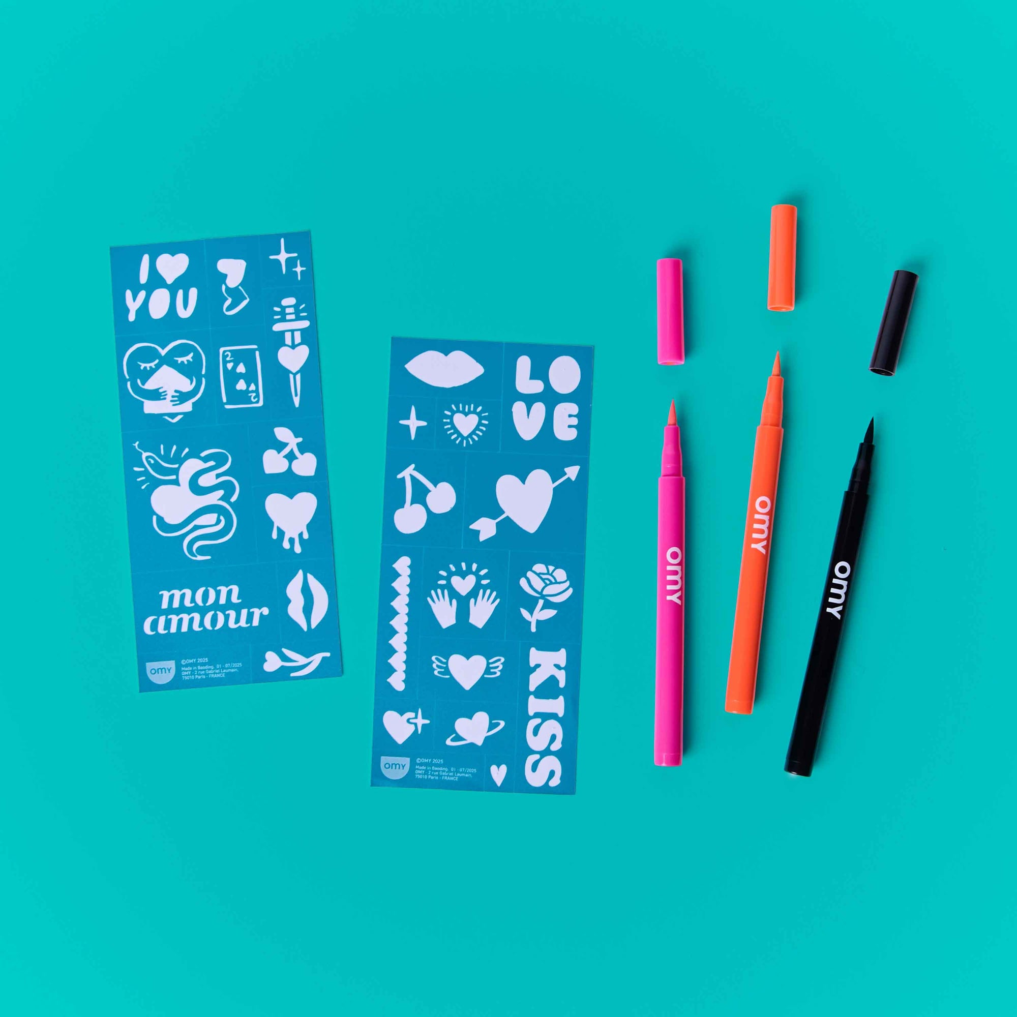 Two blue sticker sheets with white designs and four colorful markers on a teal background.