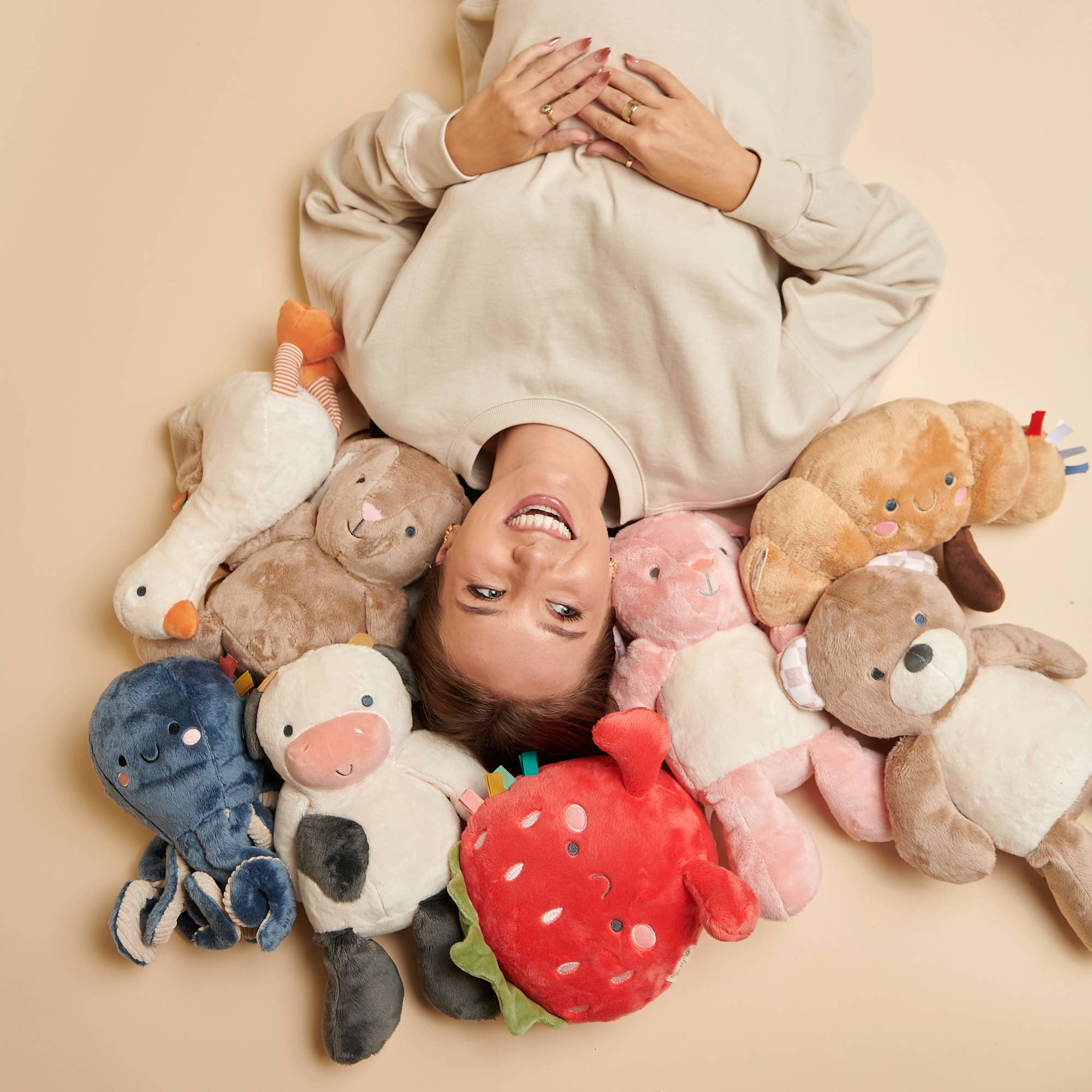 Person lying on a beige surface surrounded by colorful plush toys