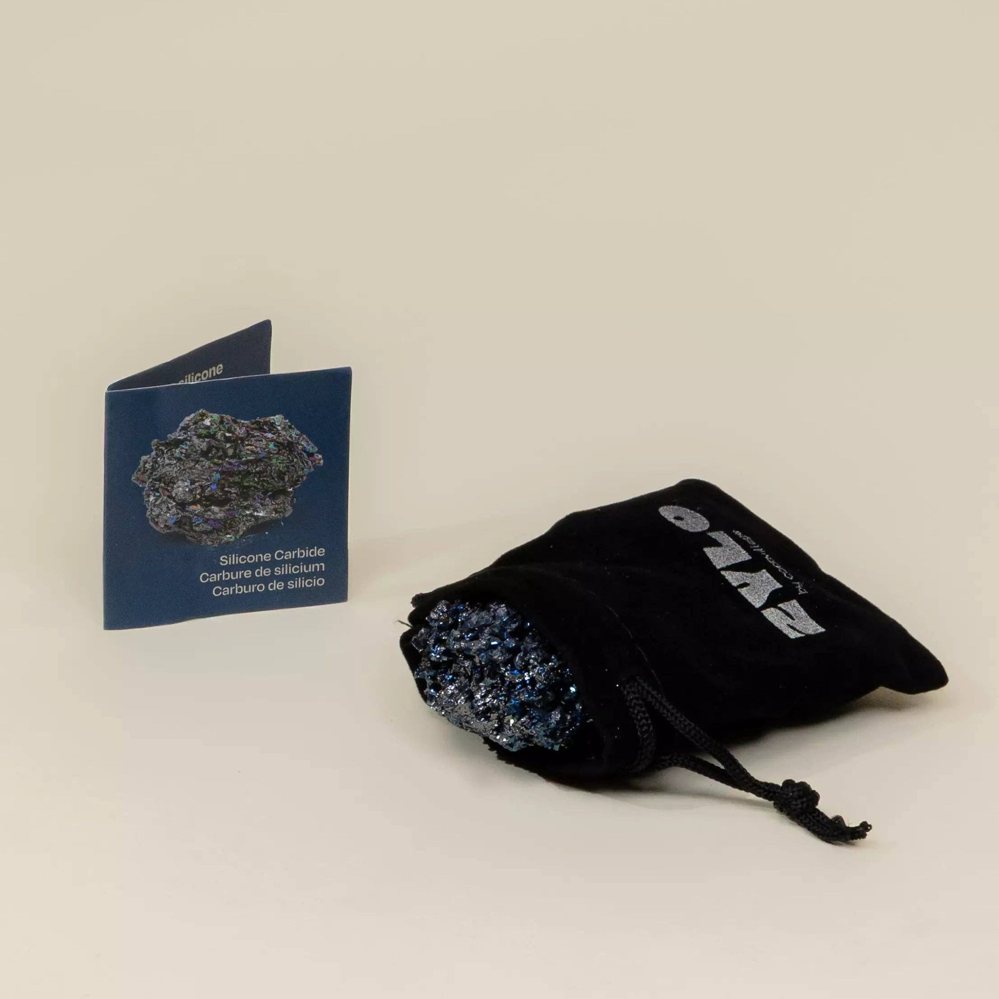 Black drawstring bag with crystals, blue card, and black box on a beige background