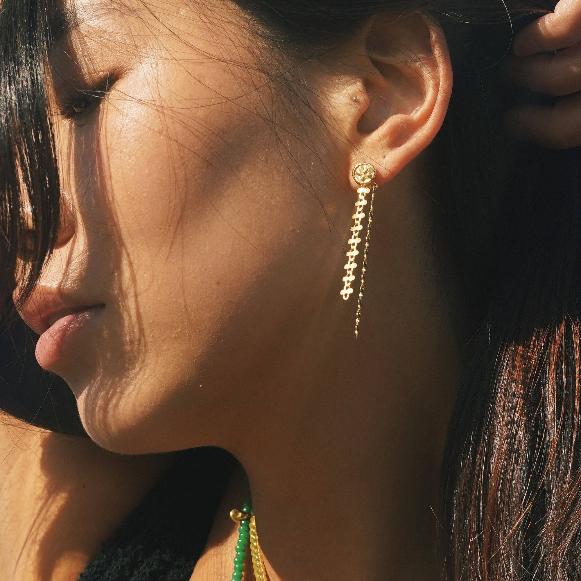 Close-up of a woman wearing gold earrings with green beads.