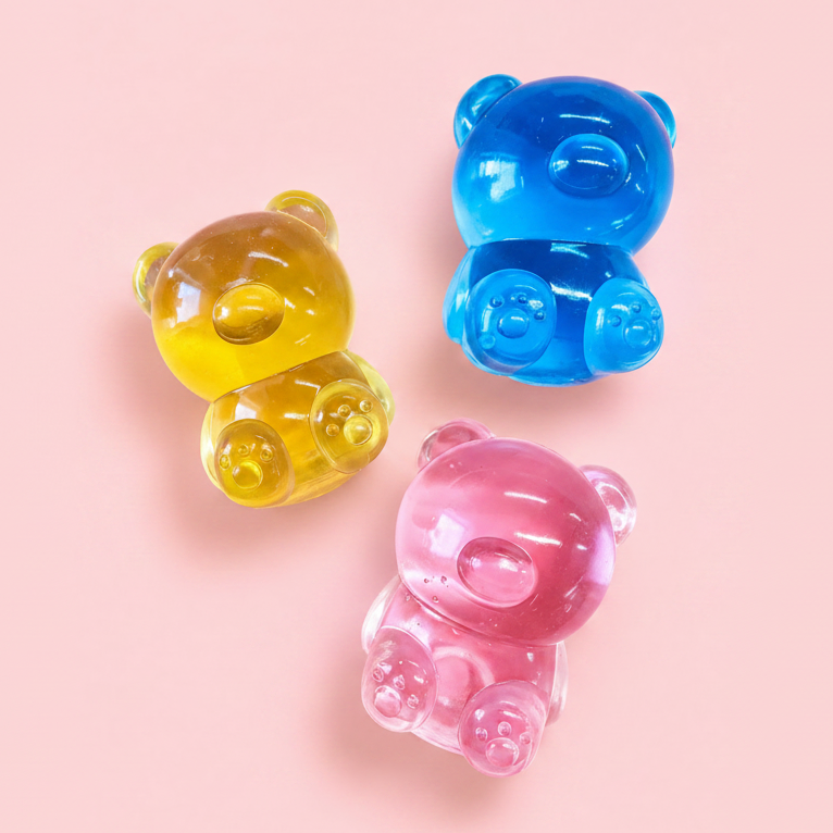 Three translucent gummy bear-shaped items in yellow, blue, and pink, arranged on a solid light pink background.