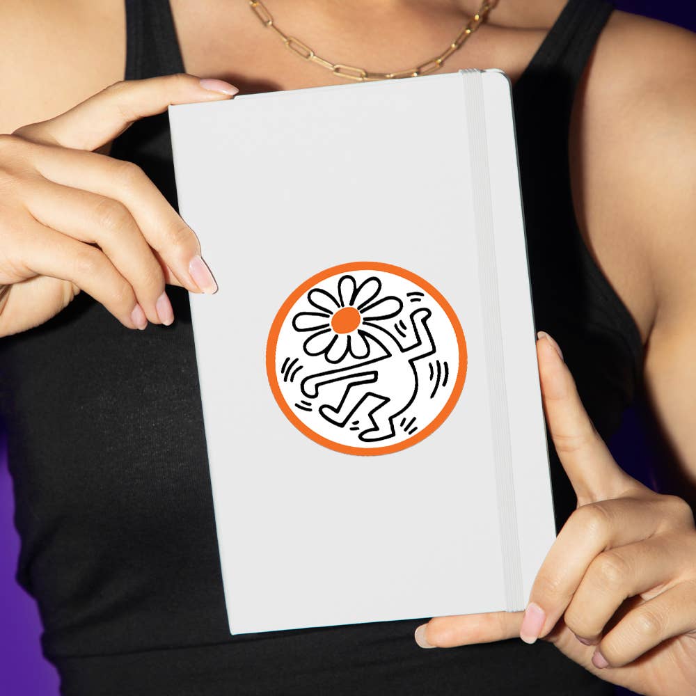 Person holding a white book with a Keith Haring-style illustration on a purple background