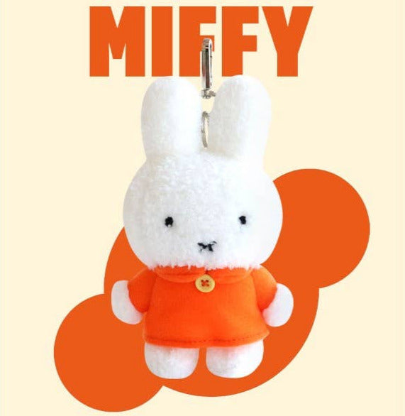 Plush keychain of a white character in an orange outfit with 'MIFFY' text above on a beige background