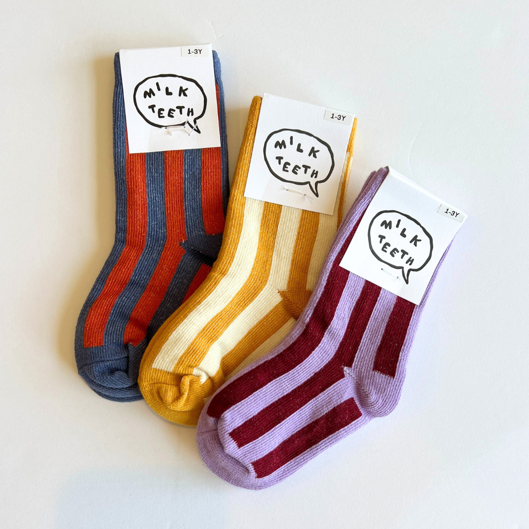 Three pairs of striped socks with 'Milk Teeth' labels on a light background