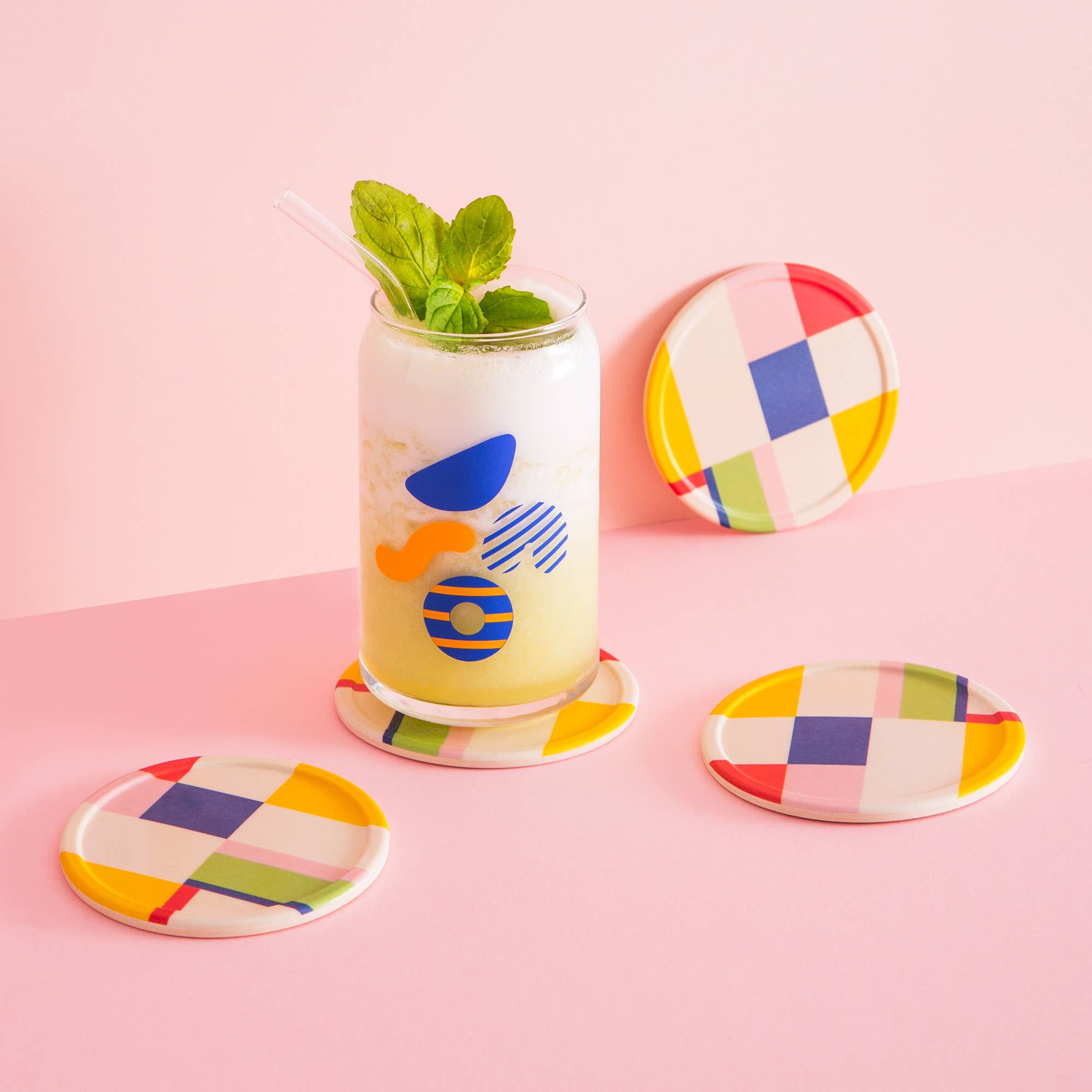 Glass of lemonade with mint leaves on a pink surface, surrounded by colorful coasters.