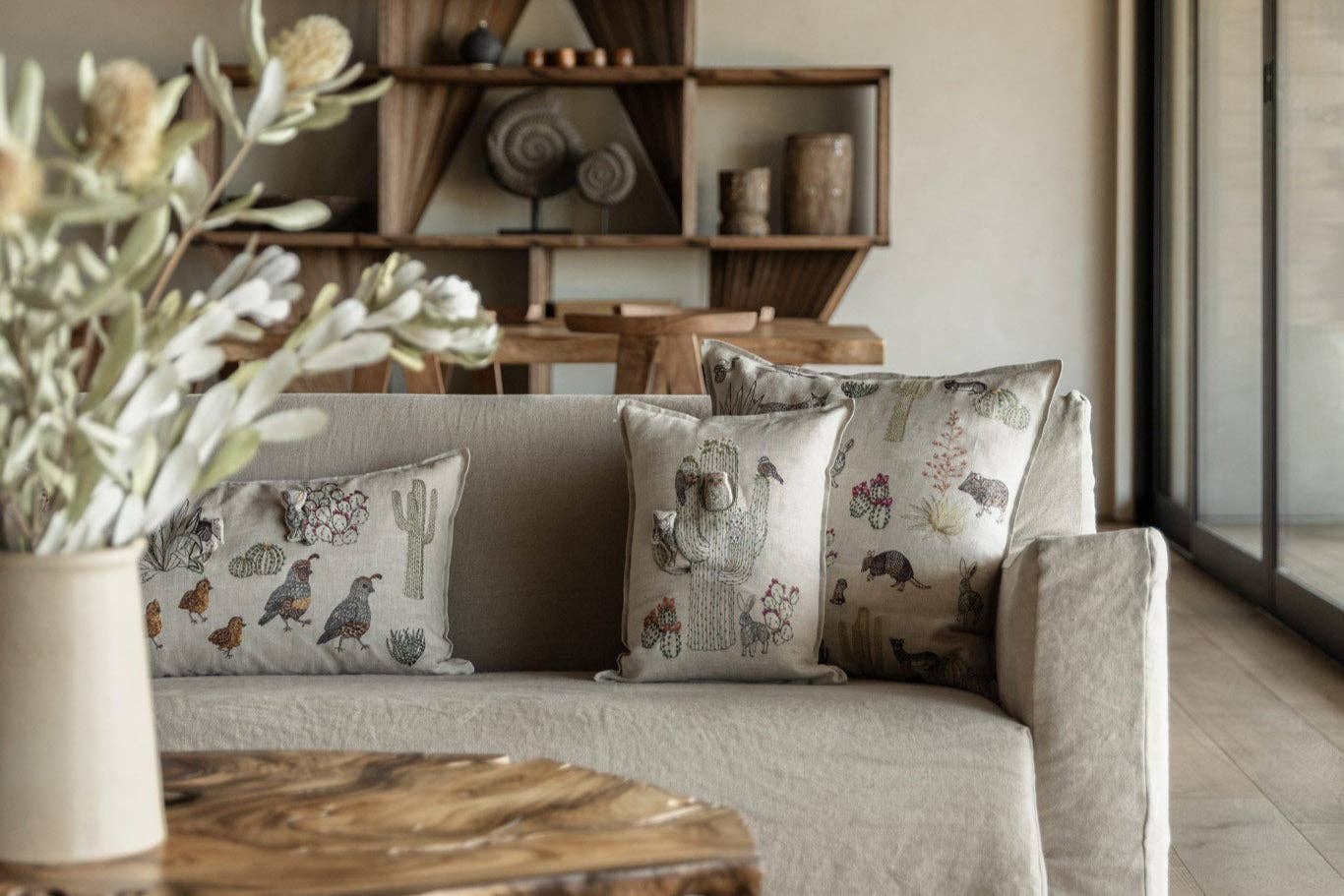 Three decorative throw pillows with detailed vintage-style animal and botanical prints in muted earthy tones, styled on a light beige sofa in a modern living room setting.