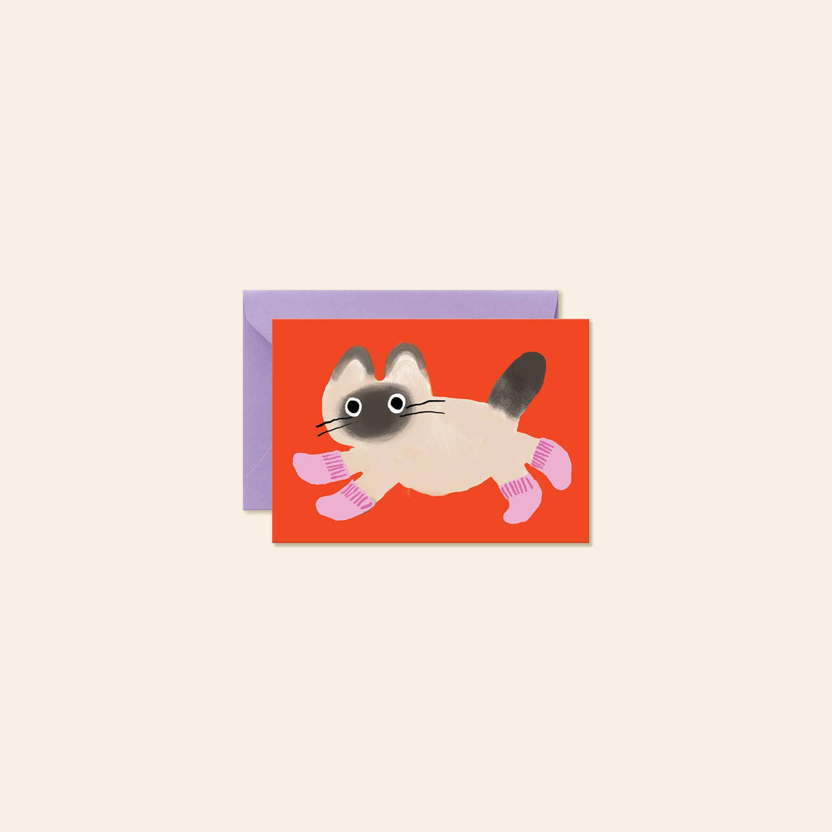 A greeting card featuring a cartoon Siamese cat with pink socks on a bright red background, shown with a lavender envelope behind it on a light beige background.