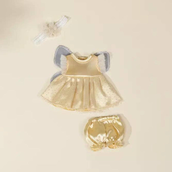 A baby angel outfit set laid flat on a warm cream background, including a gold satin dress with light blue wings, matching gold diaper cover, and a small white bow headband.