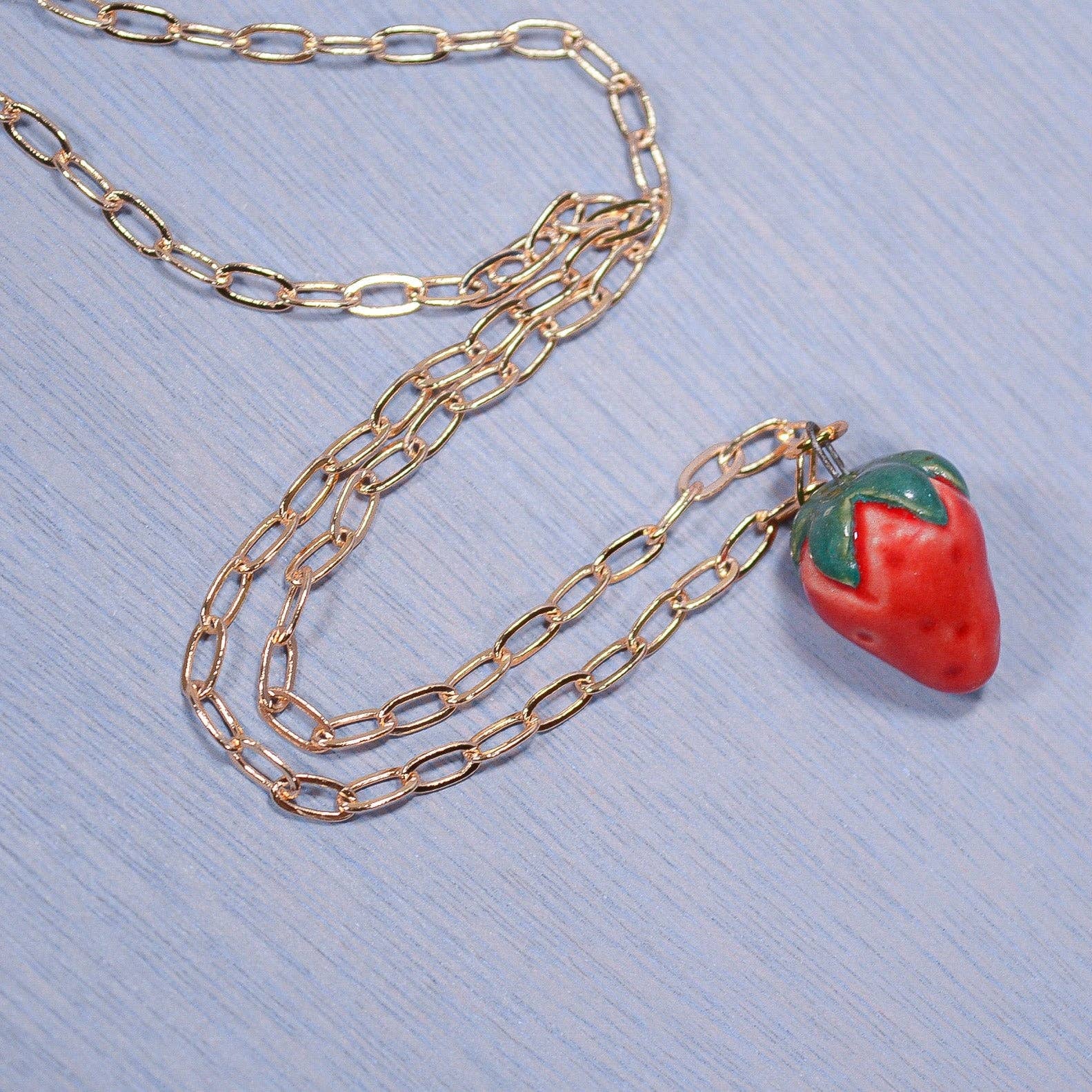 Gold chain necklace with a strawberry-shaped pendant on a blue textured background
