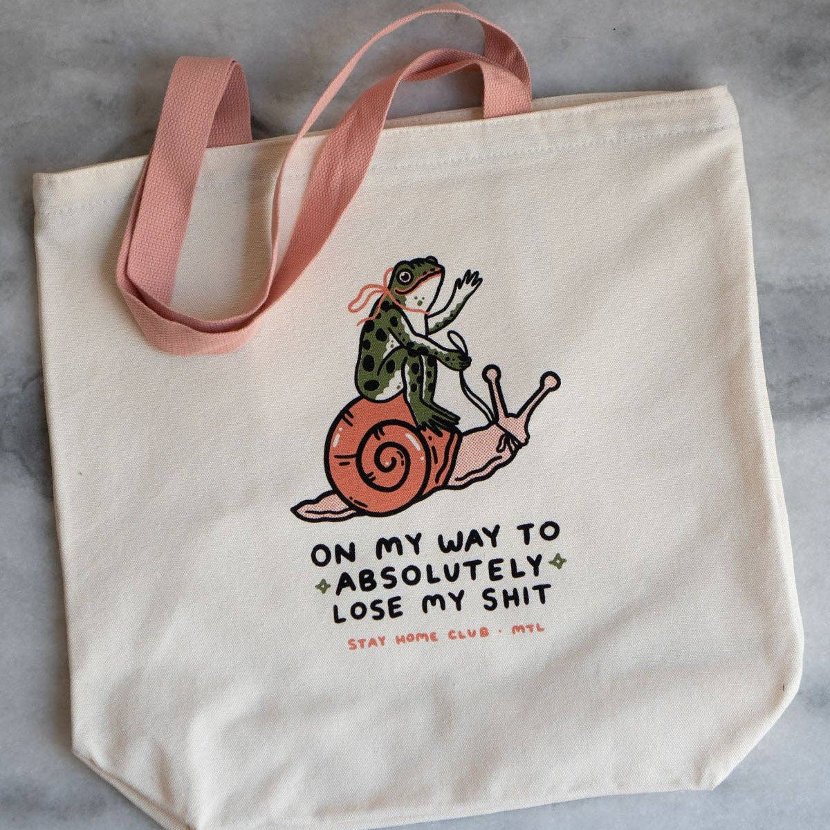 Tote bag with a frog on a snail illustration and humorous text on a gray background