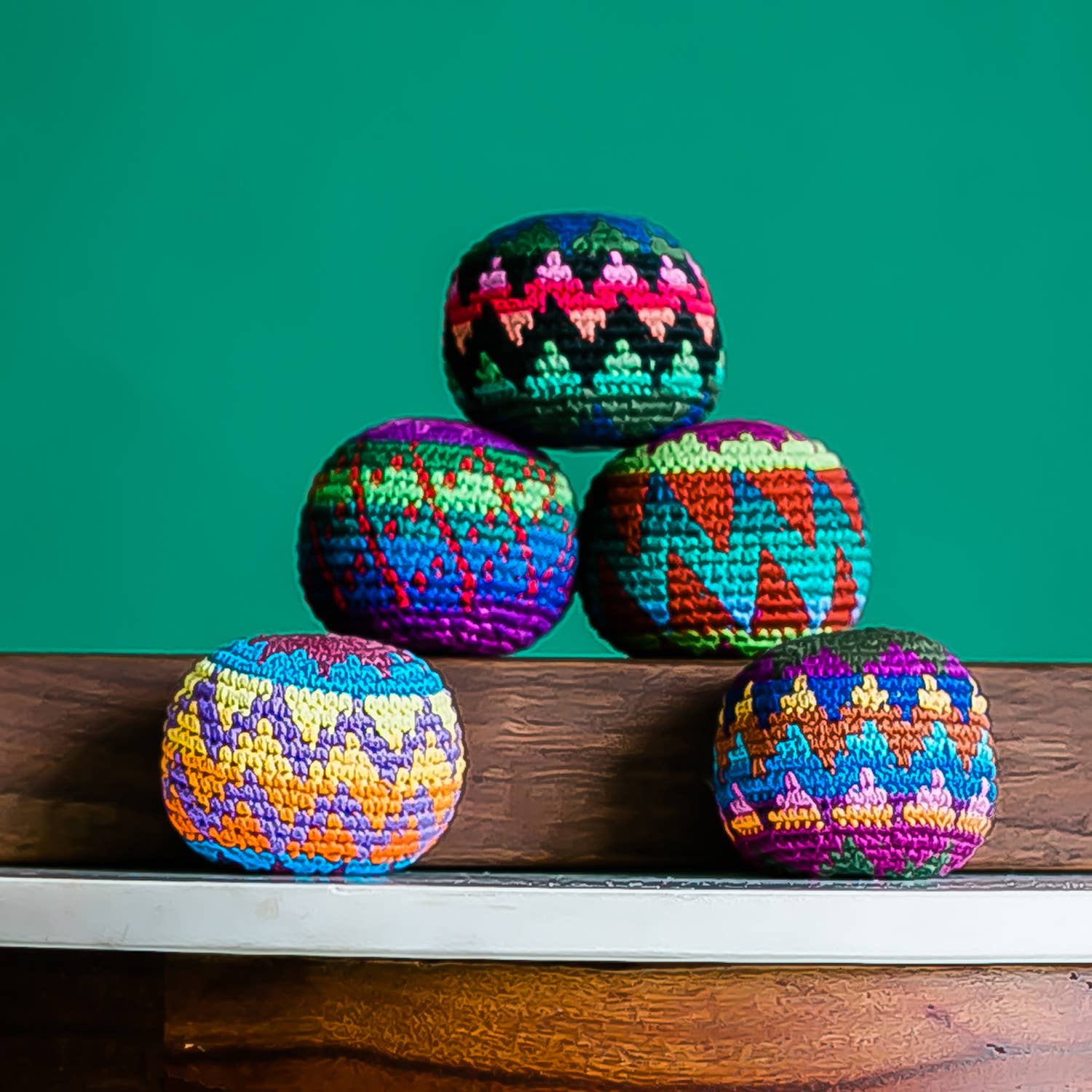 Colorful crocheted balls stacked on a wooden surface with a green background