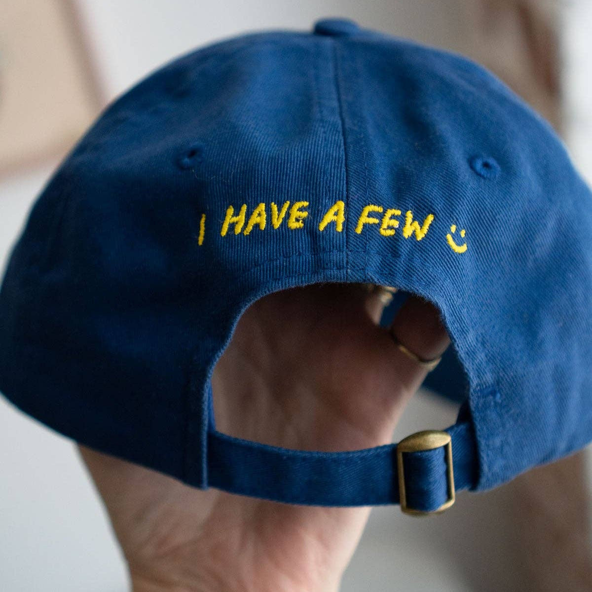 Blue cap with yellow text held by a hand against a blurred background