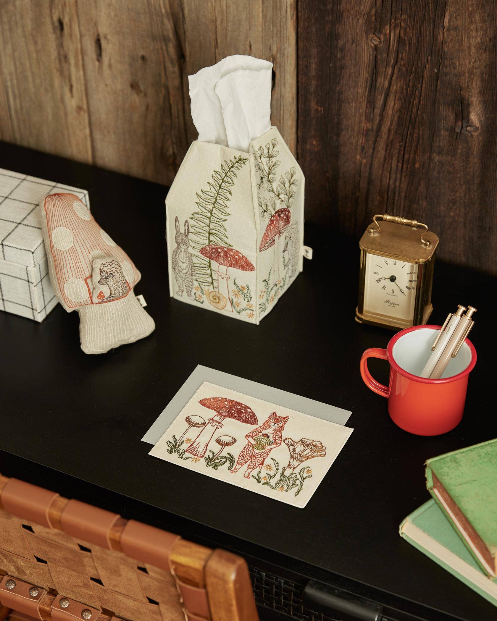 Decorative tissue box with nature-themed design on a wooden surface with stationery items.
