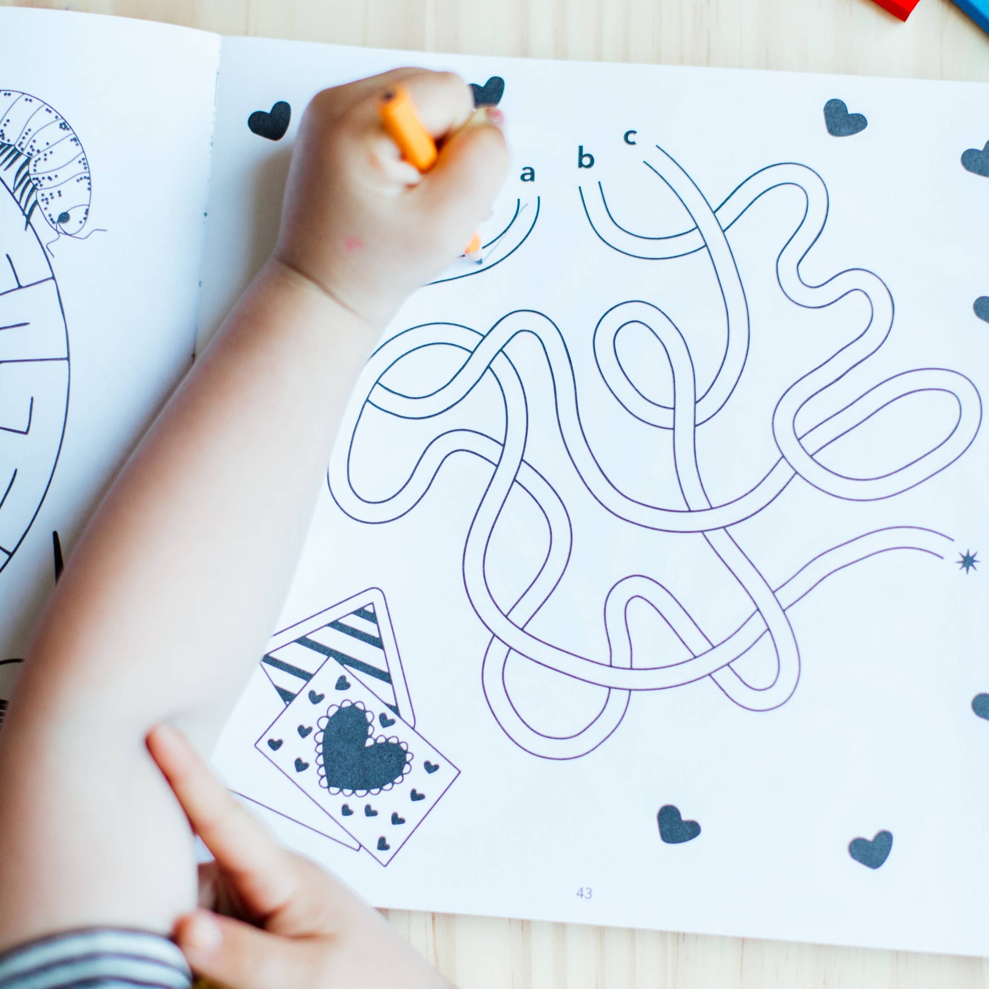 Child coloring a maze on a coloring book with colored pencils.