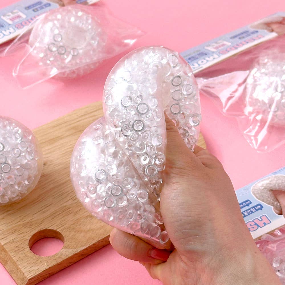 Hand holding a clear gel ball with embedded beads on a pink background