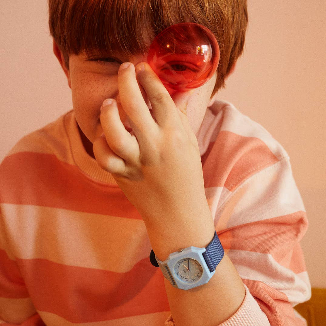 Person wearing a striped sweater and blue watch, holding a red object to their face against a plain background