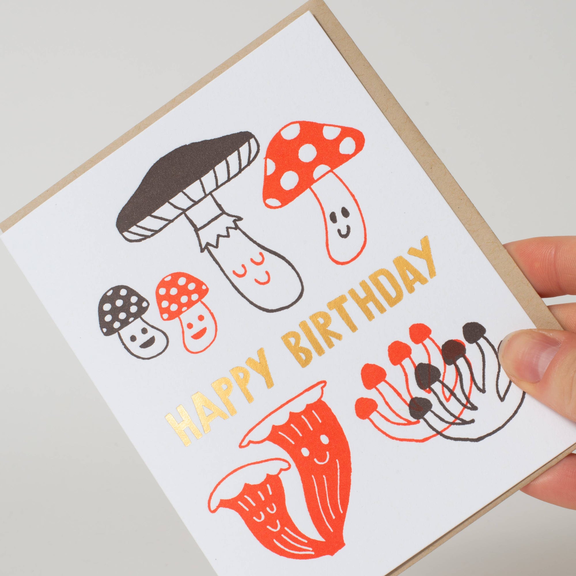 Greeting card with mushroom illustrations and 'Happy Birthday' text held by a hand.
