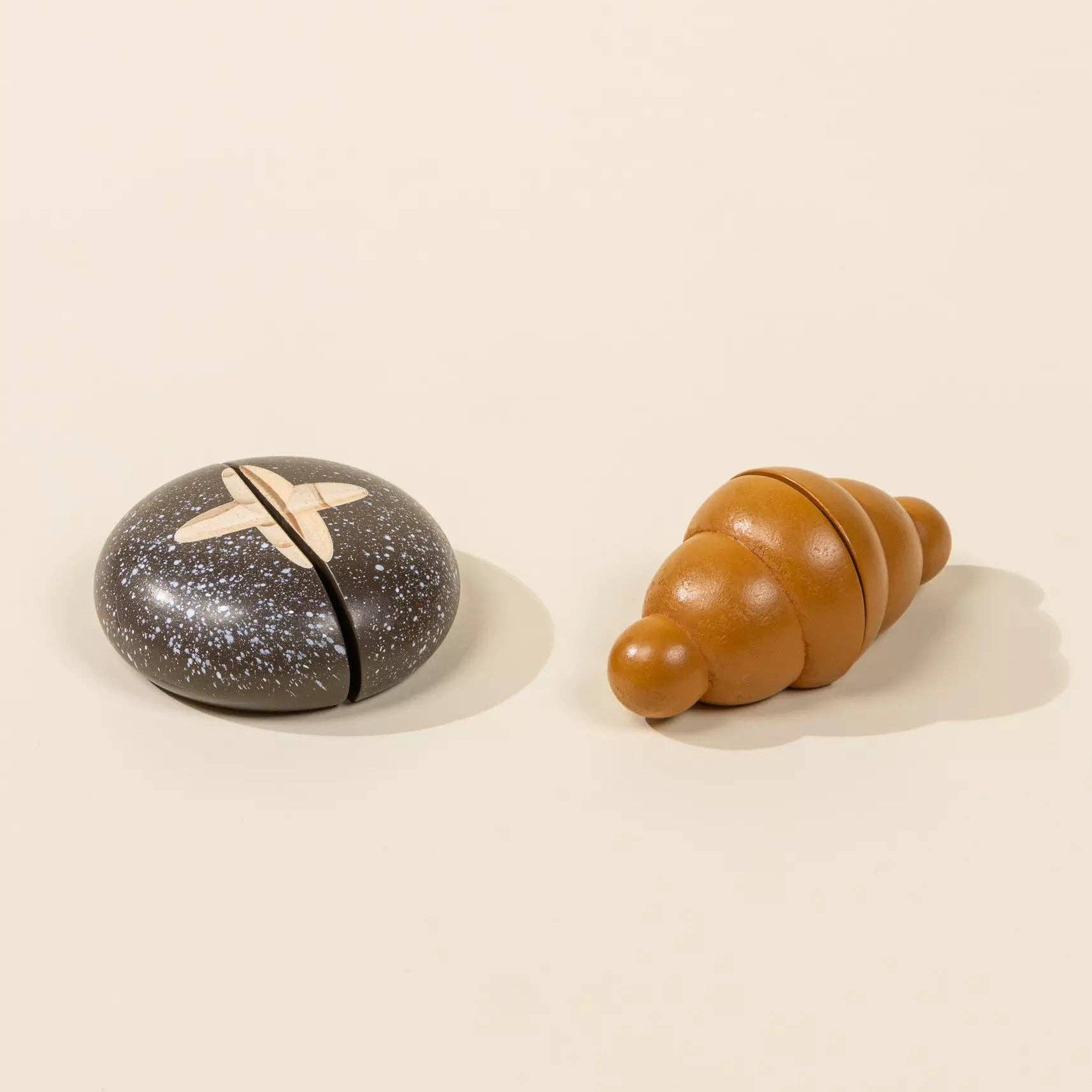 Two wooden toys, one speckled gray and black, the other brown, on a beige background.