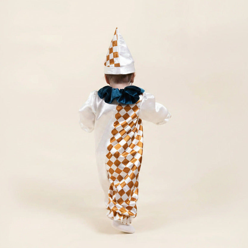A child shown from the back wearing a white clown costume with a gold and white harlequin pattern down the back, a dark blue ruffled collar, and a matching pointed hat, against a plain beige studio background.
