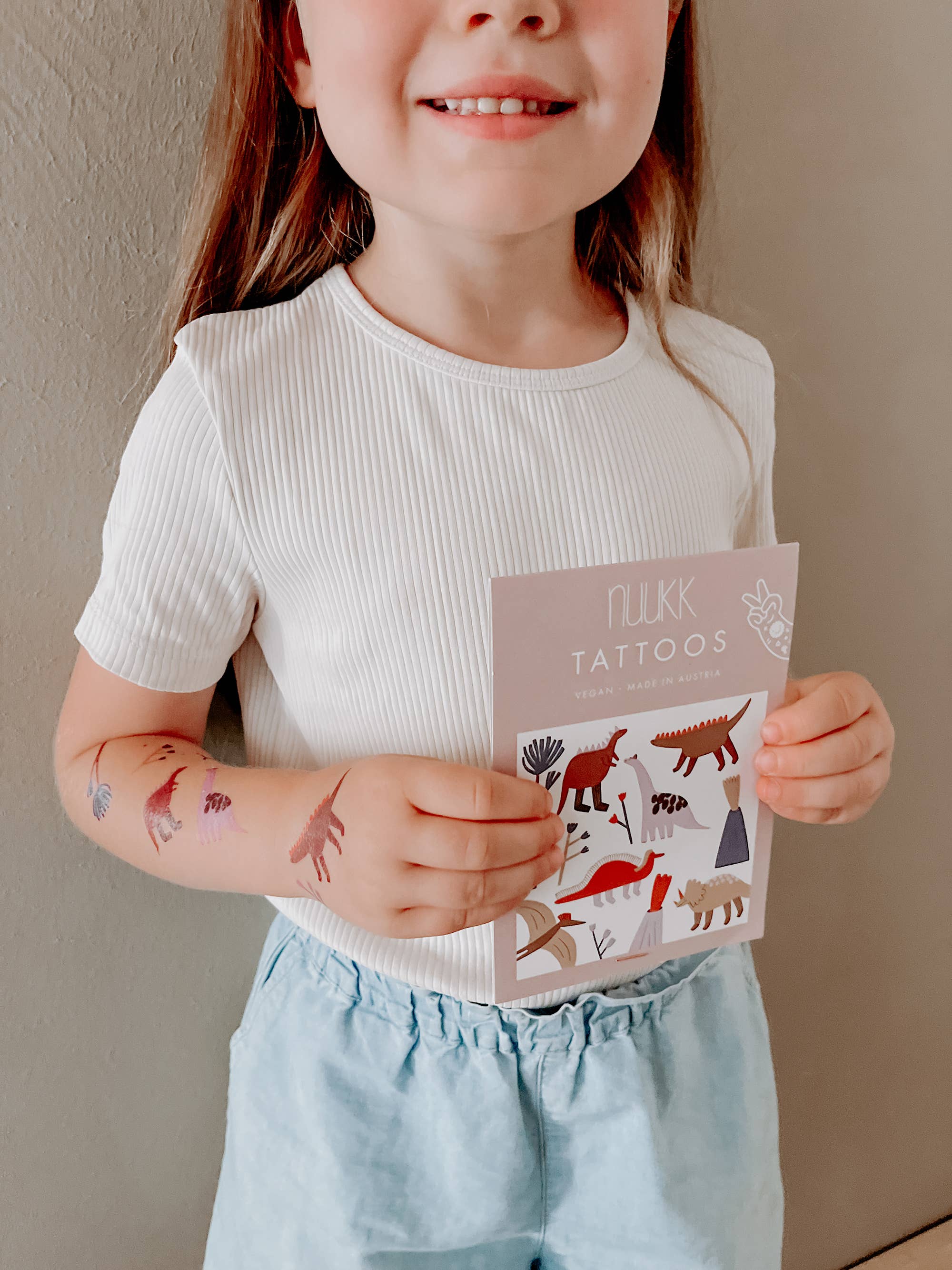 Child with temporary tattoos holding a book of tattoos against a plain background