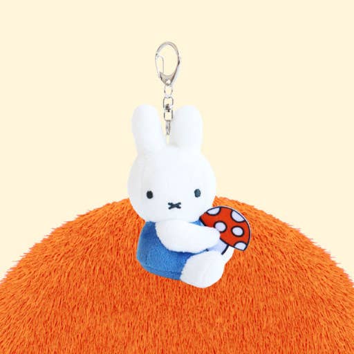 Plush keychain of a white rabbit character holding a mushroom on an orange ball with a beige background