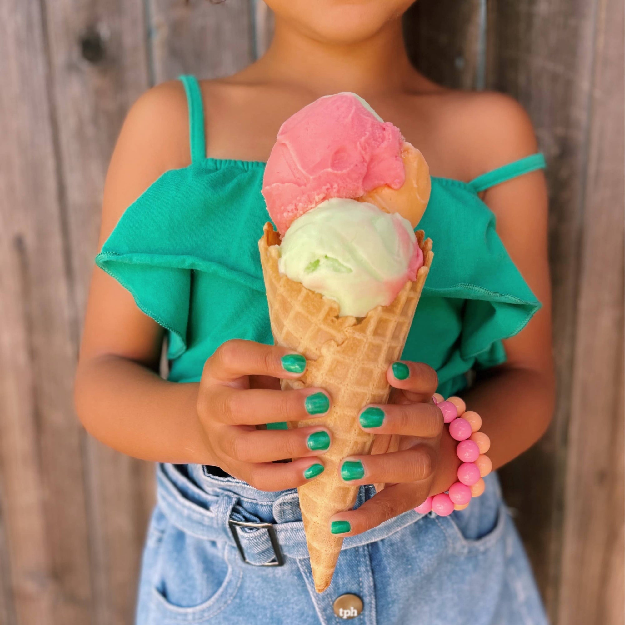 Person holding a pink and green ice cream cone against a wooden background
