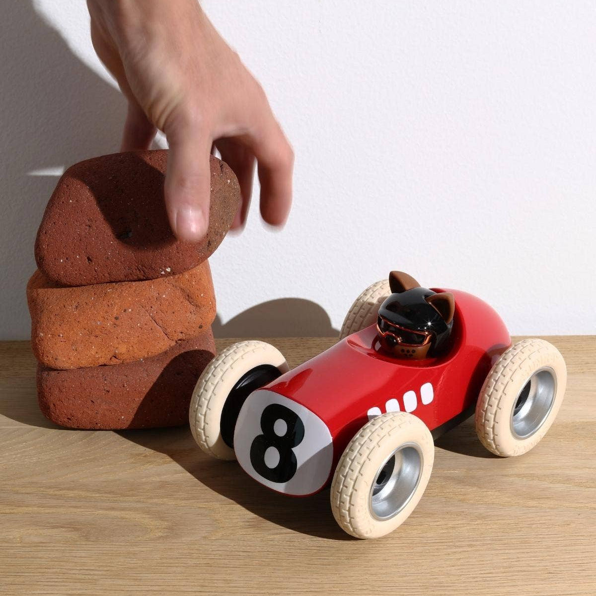 Red toy race car with number 8 on a wooden surface, being pushed by a hand.