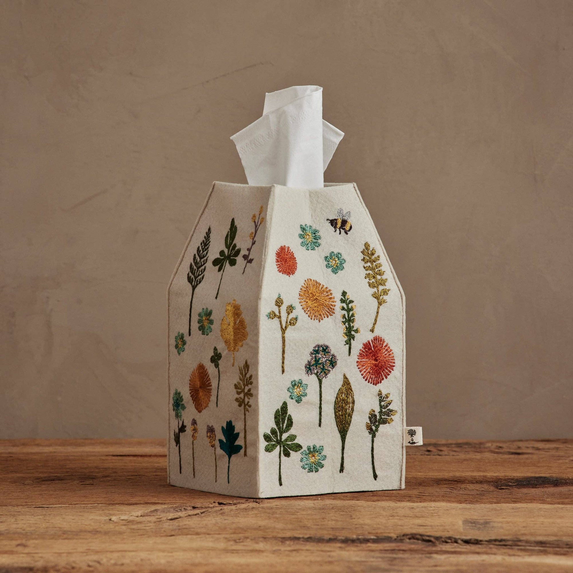 Tissue box cover with floral designs on a wooden surface and brown background