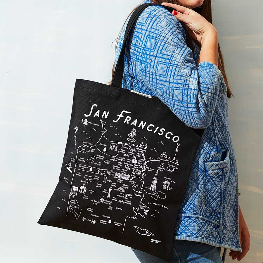 Person holding a black tote bag with 'San Francisco' design against a light background