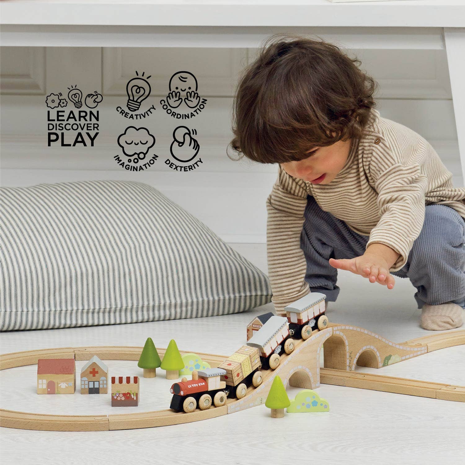 Child playing with a wooden train set on a light-colored floor.