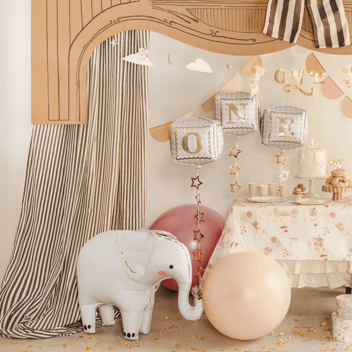 Decorative setup with balloons, a cake, and an elephant plush toy in a room.