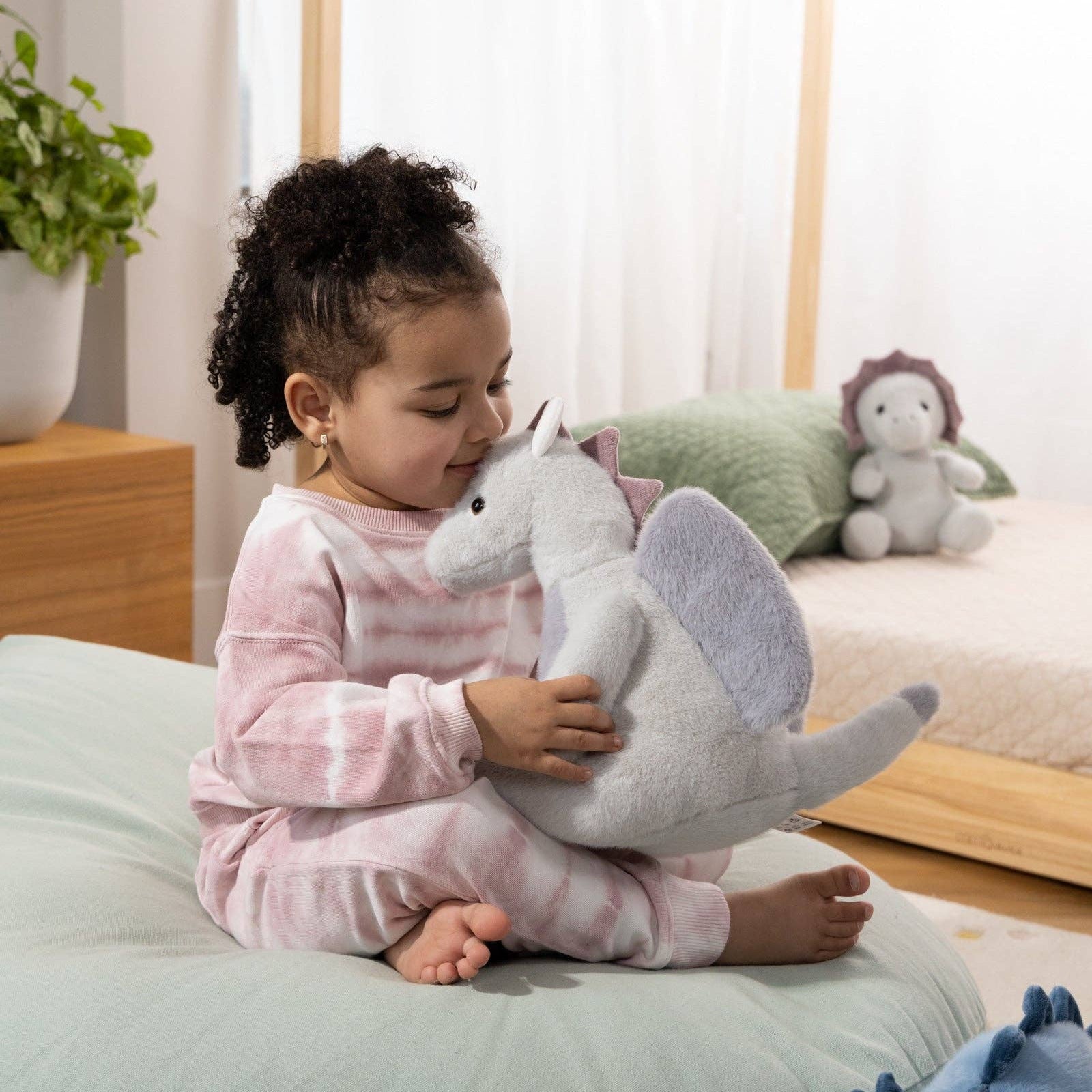Child holding a plush dinosaur toy in a cozy room with soft lighting
