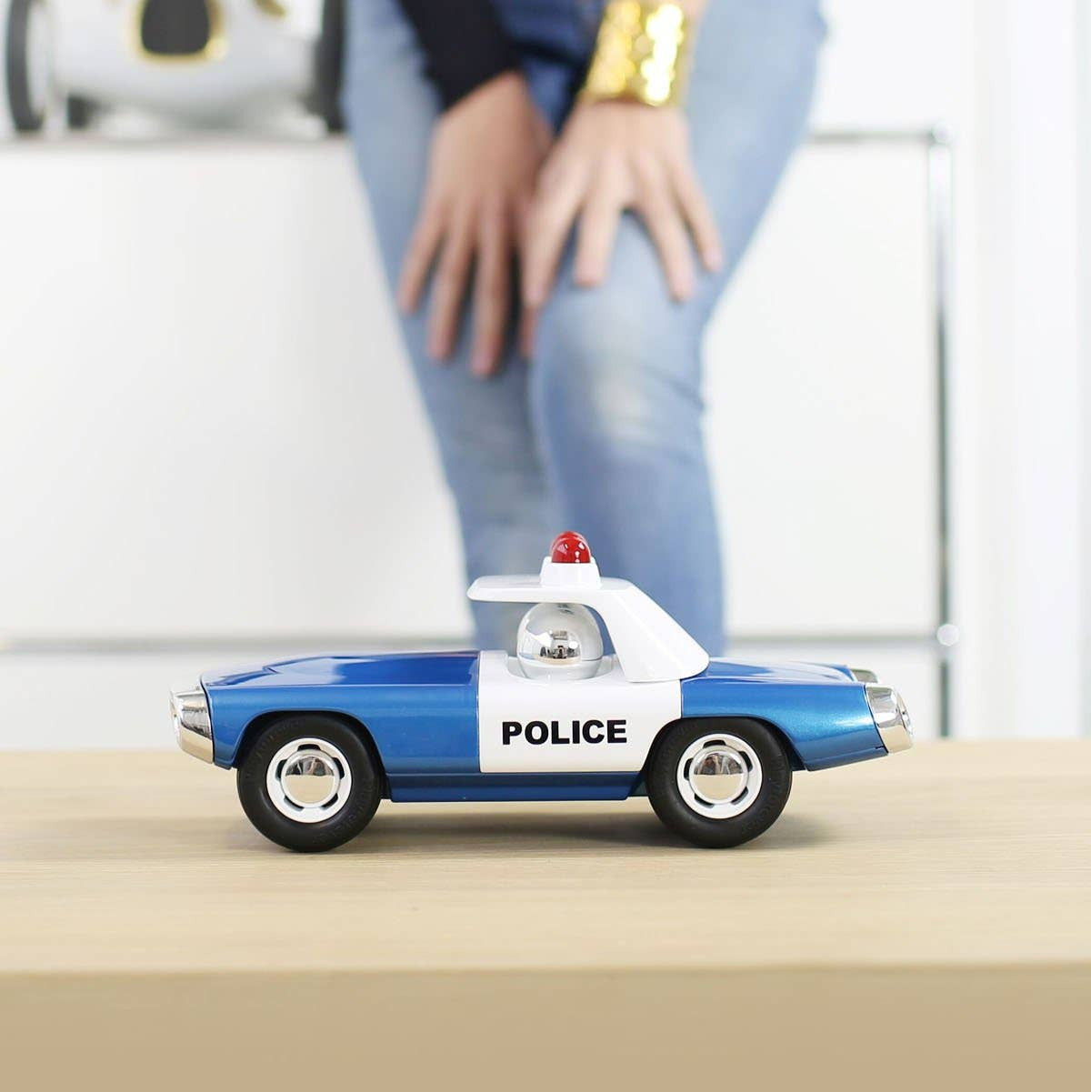 Small toy police car on a surface with a blurred person in the background