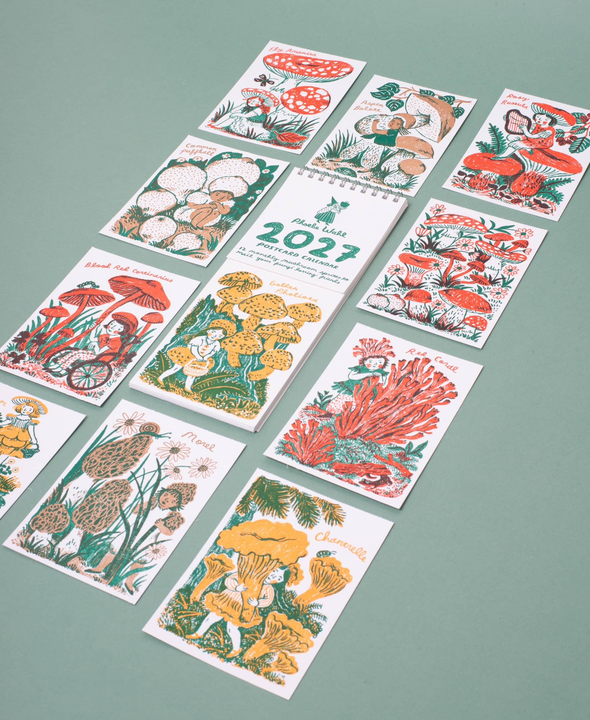 A set of illustrated cards or prints arranged on a muted green background. The cards feature colorful drawings of mushrooms, flowers, and nature scenes, with one central card showing the year 2023.