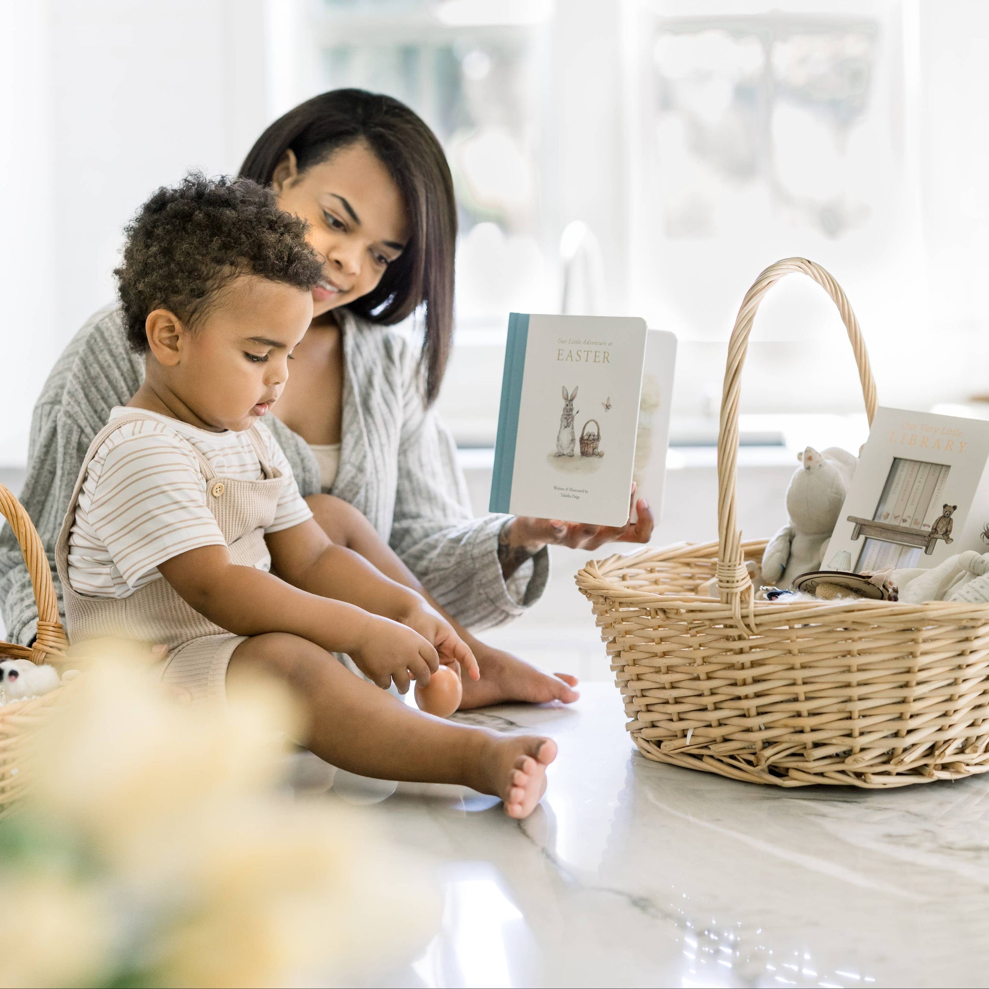 Woman and child sitting at a table with a book, surrounded by wicker baskets.