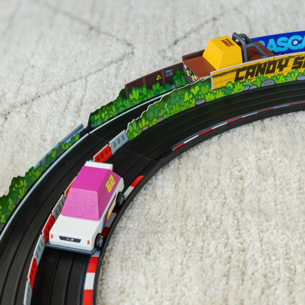Toy train set with a pink car on a track, featuring colorful scenery and branding.