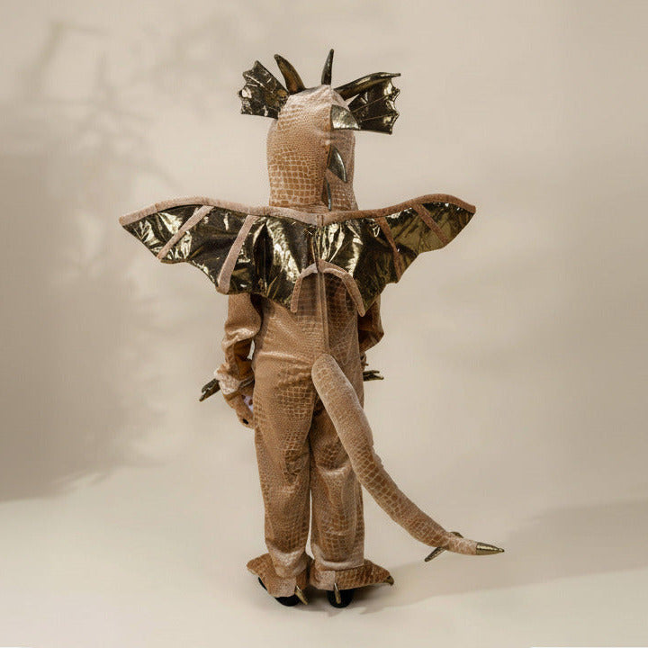 A person wearing a full-body reptile-inspired costume viewed from the back, featuring a textured tan and brown hooded suit with metallic gold bat-like wings, a long tail, and horn-like head details against a plain light beige studio background.