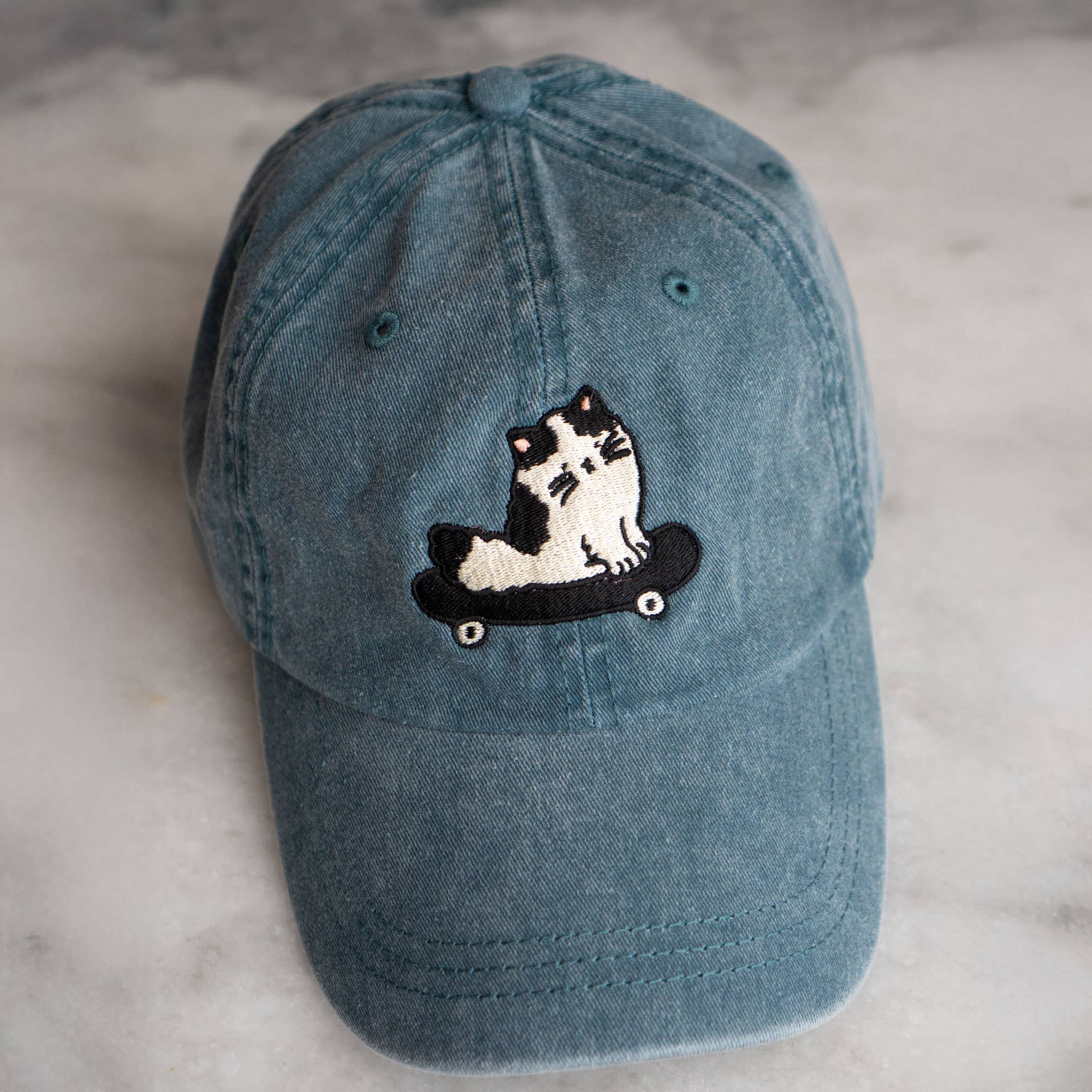 Blue denim cap with a cat on a skateboard patch on a marble surface
