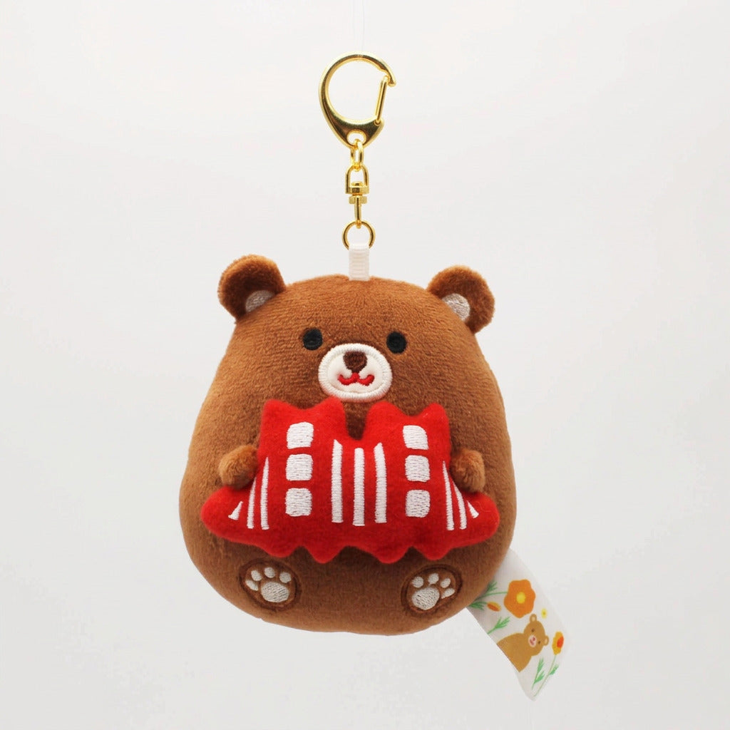 A brown plush bear keychain or bag charm holding a red and white striped scarf, attached to a black strap and gold clasp, photographed on a clean white background.