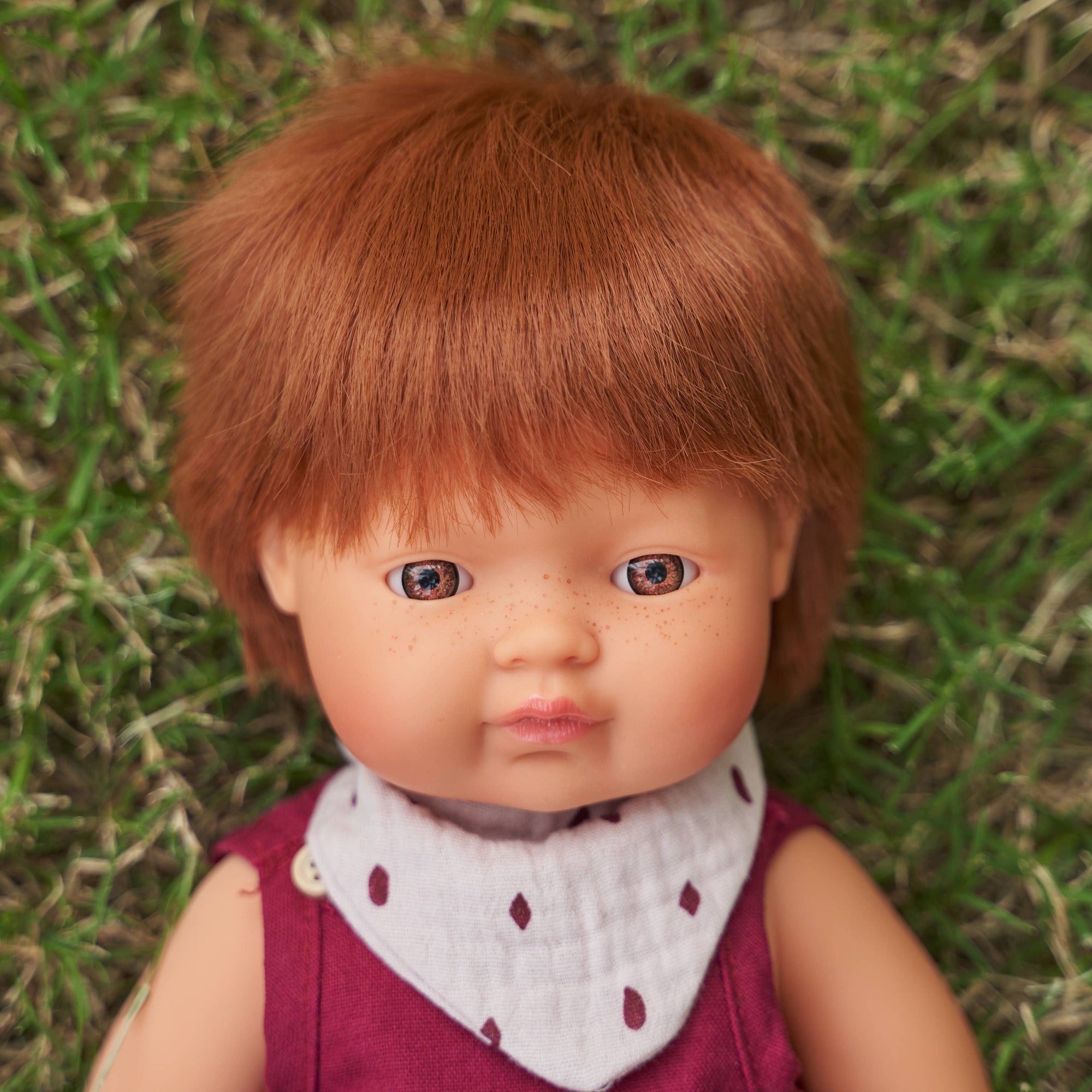 Doll with red hair and a purple outfit sitting on grass