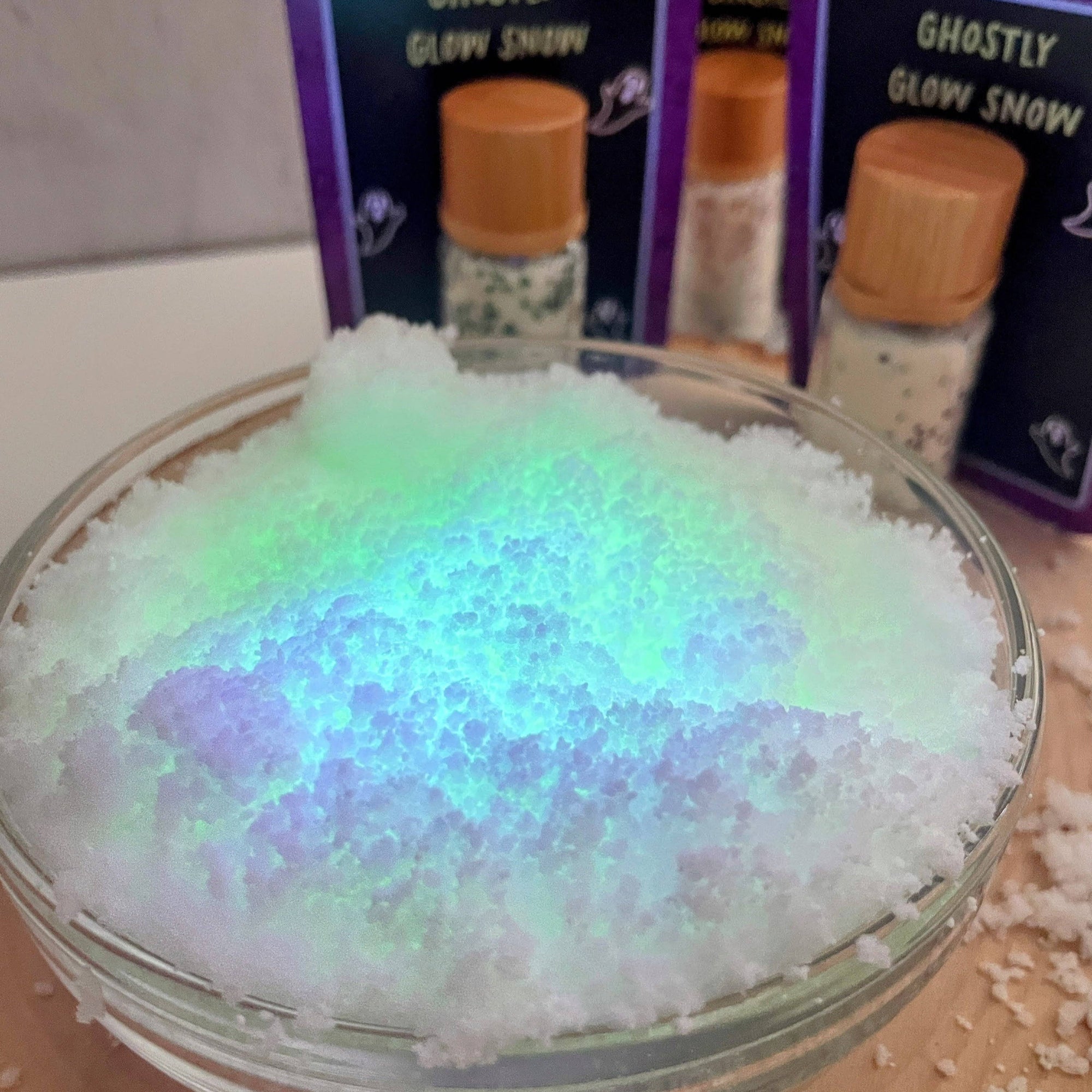Glowing snow in a glass bowl with 'Ghostly Glow Snow' packaging in the background.