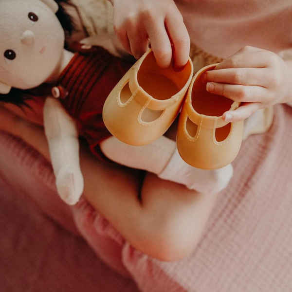 child holding up orange doll shoes over doll