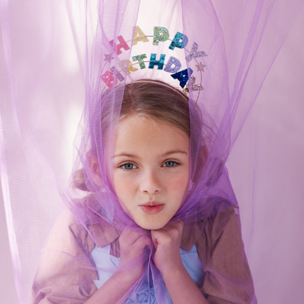 girl wearing headband with glitterd words above it that spell out HAPPY BIRTHDAY in pastel colors