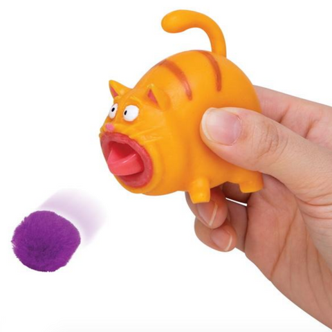 orange striped cat being squeezed with tongue out and a flying purple pompom